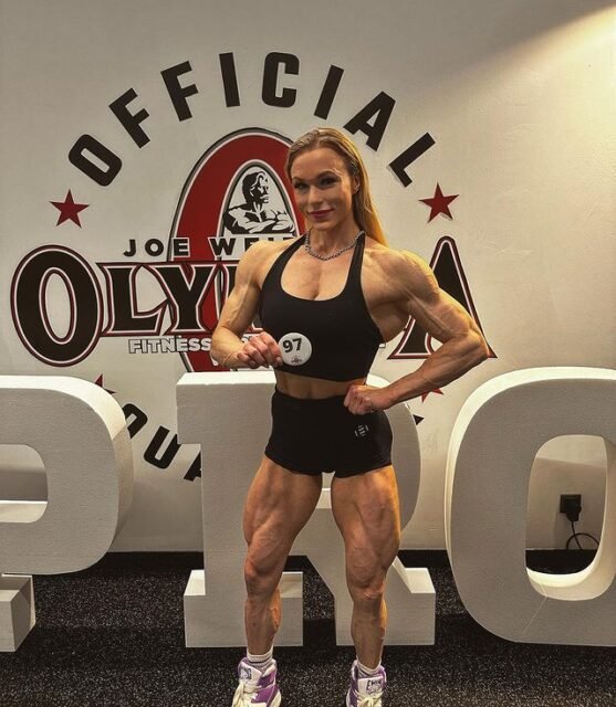 Bodybuilder posing in front of Olympia Fitness Weekend branding, wearing number 97 and black sportswear
